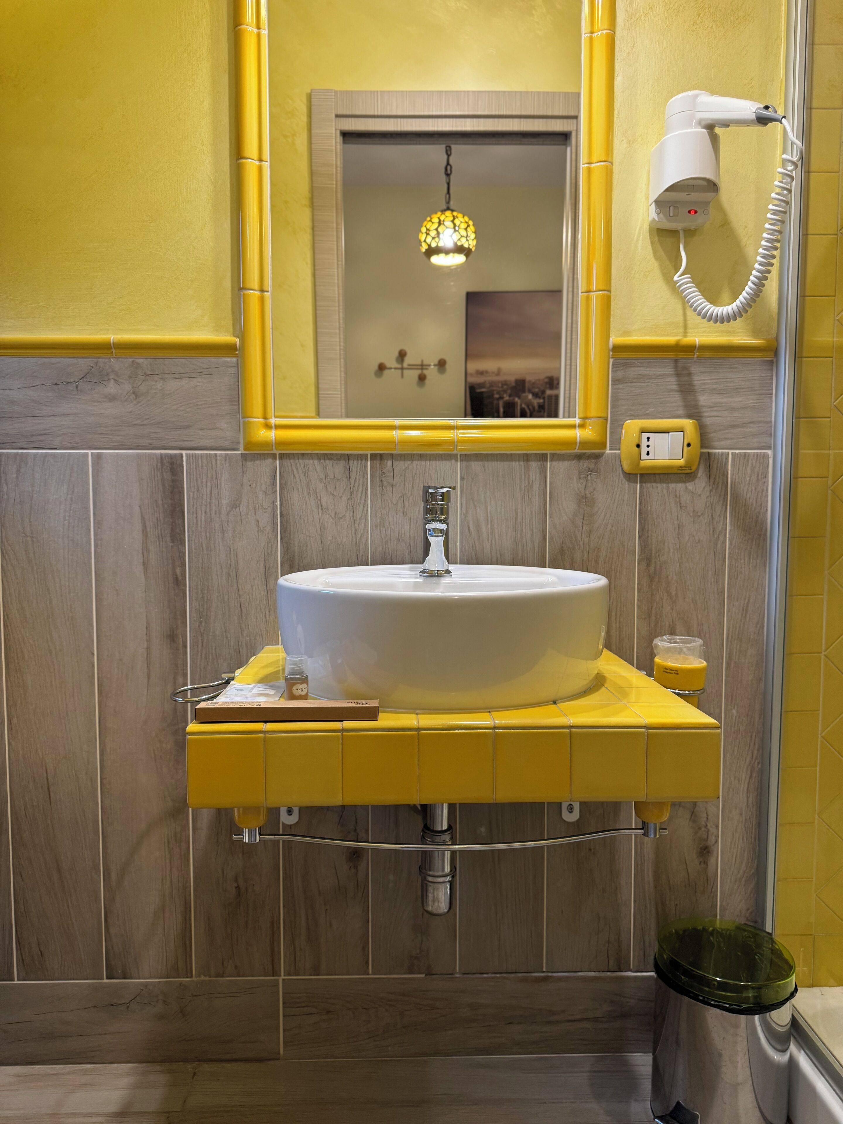 Une salle de bain avec un lavabo jaune, un miroir, un sèche-cheveux et une bouteille de shampoing.