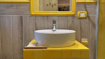 Un baño con un lavabo amarillo, un espejo, un secador de pelo y una botella de champú.
