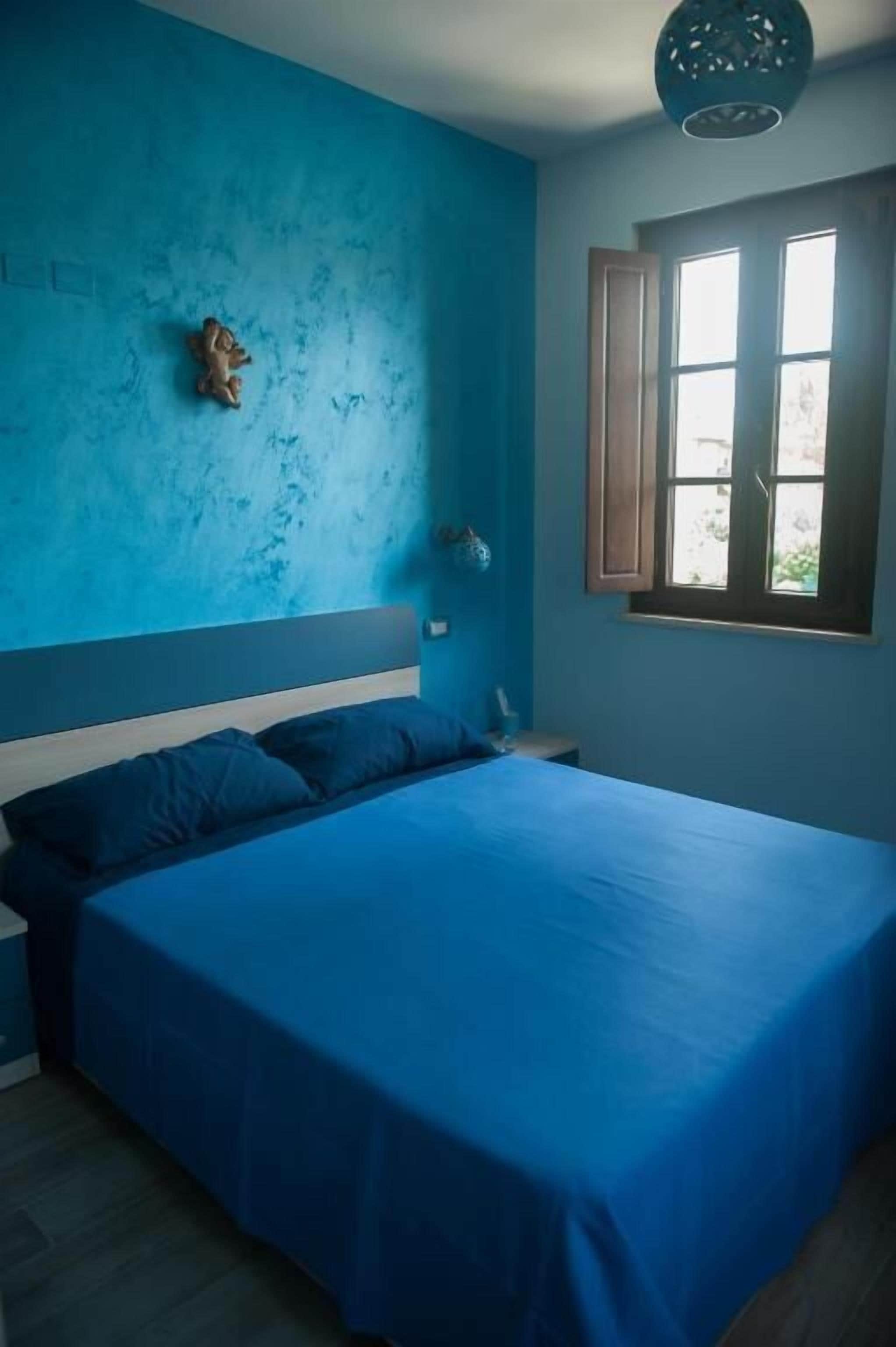 A bedroom with a large bed, a blue wall, and a window with wooden shutters.