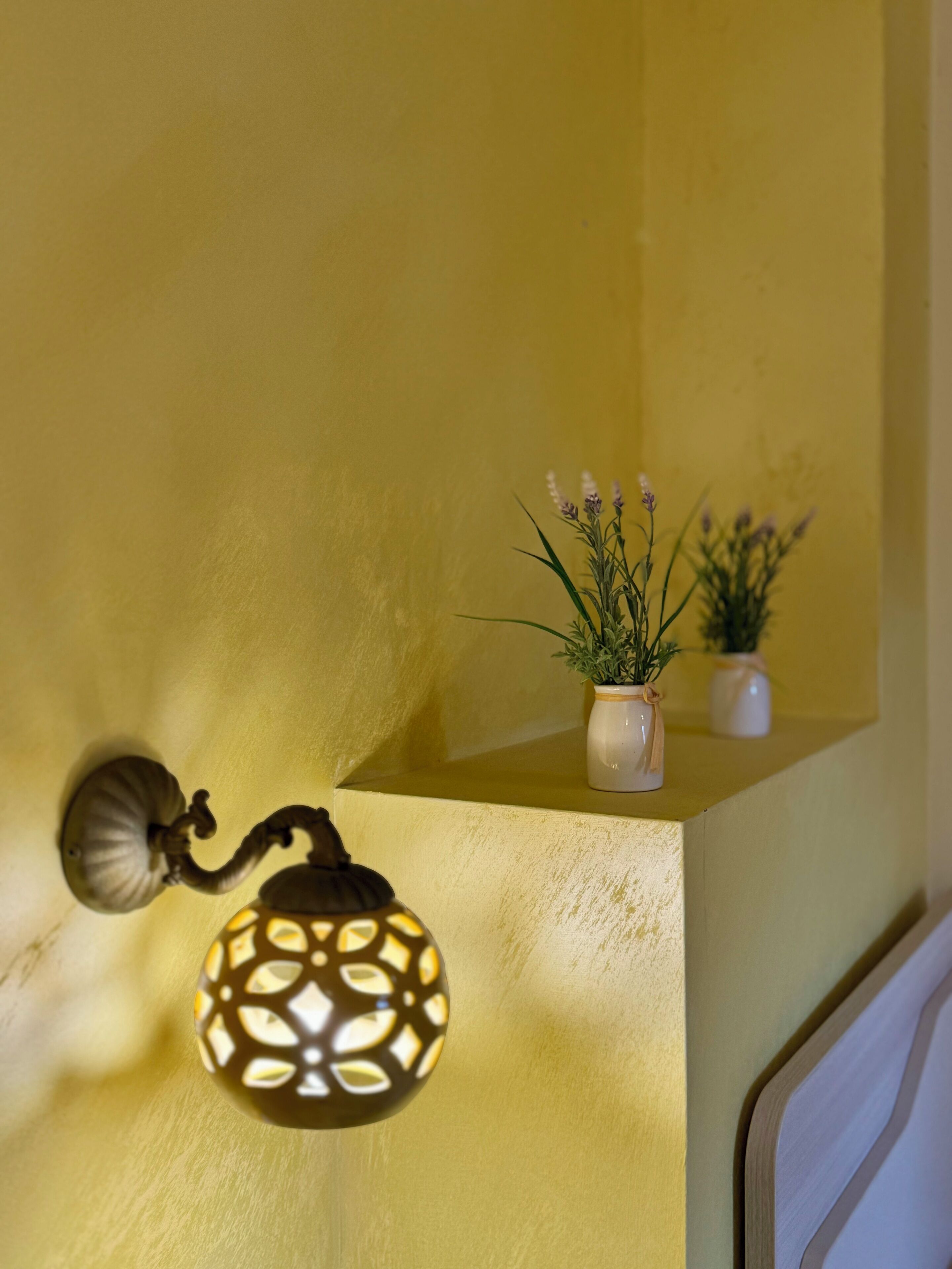 Een aan de muur bevestigde lantaarn met decoratief ontwerp, een kleine potplant en een structuurmuur.
