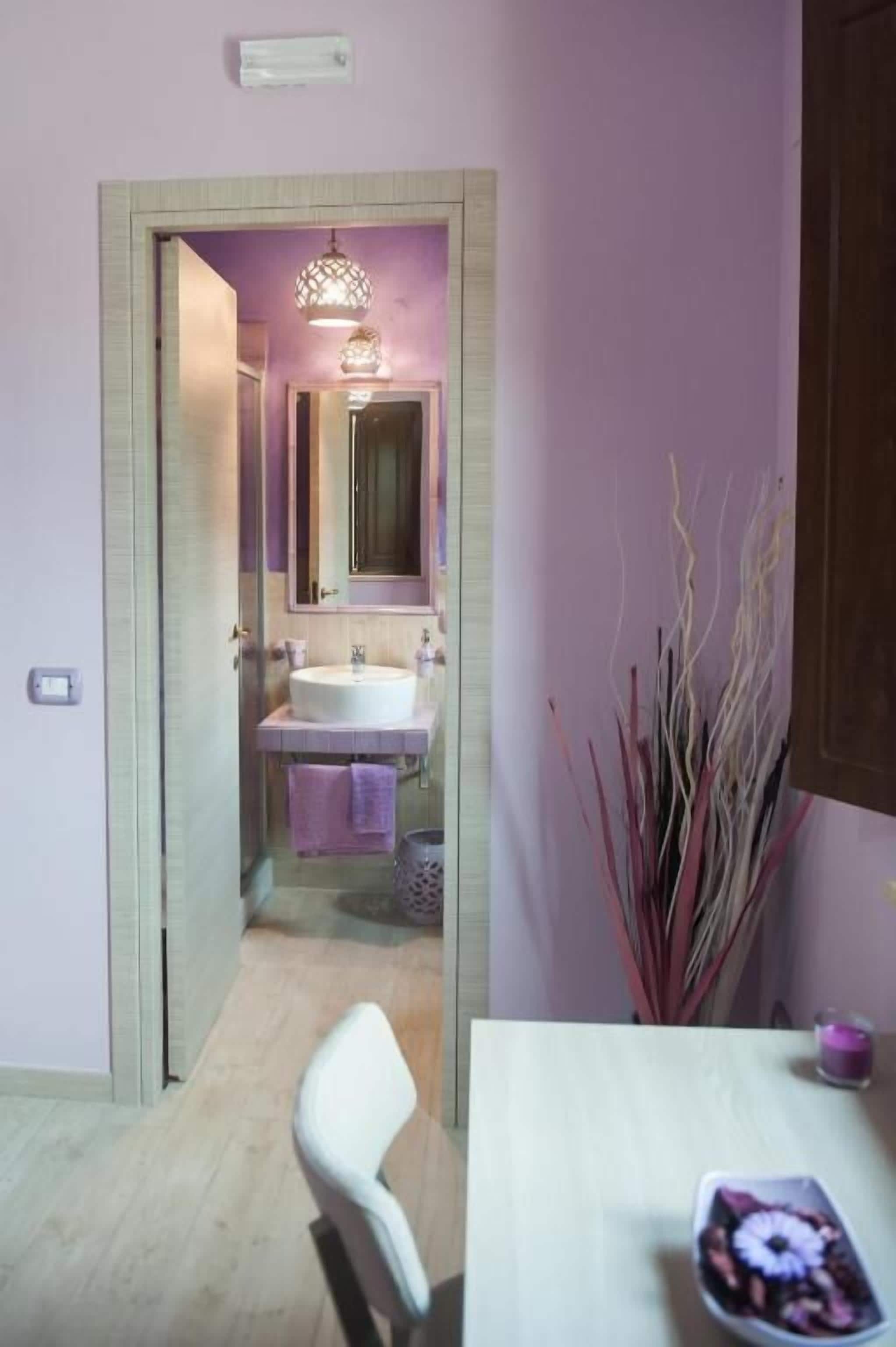 A bathroom with a glass door leading to a shower area, a sink with a mirror, and a vase with decorative branches.