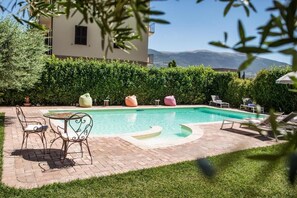 A swimming pool with a tiled deck, surrounded by greenery and a building in the background. - Domus Angeli Camere (Assisi)