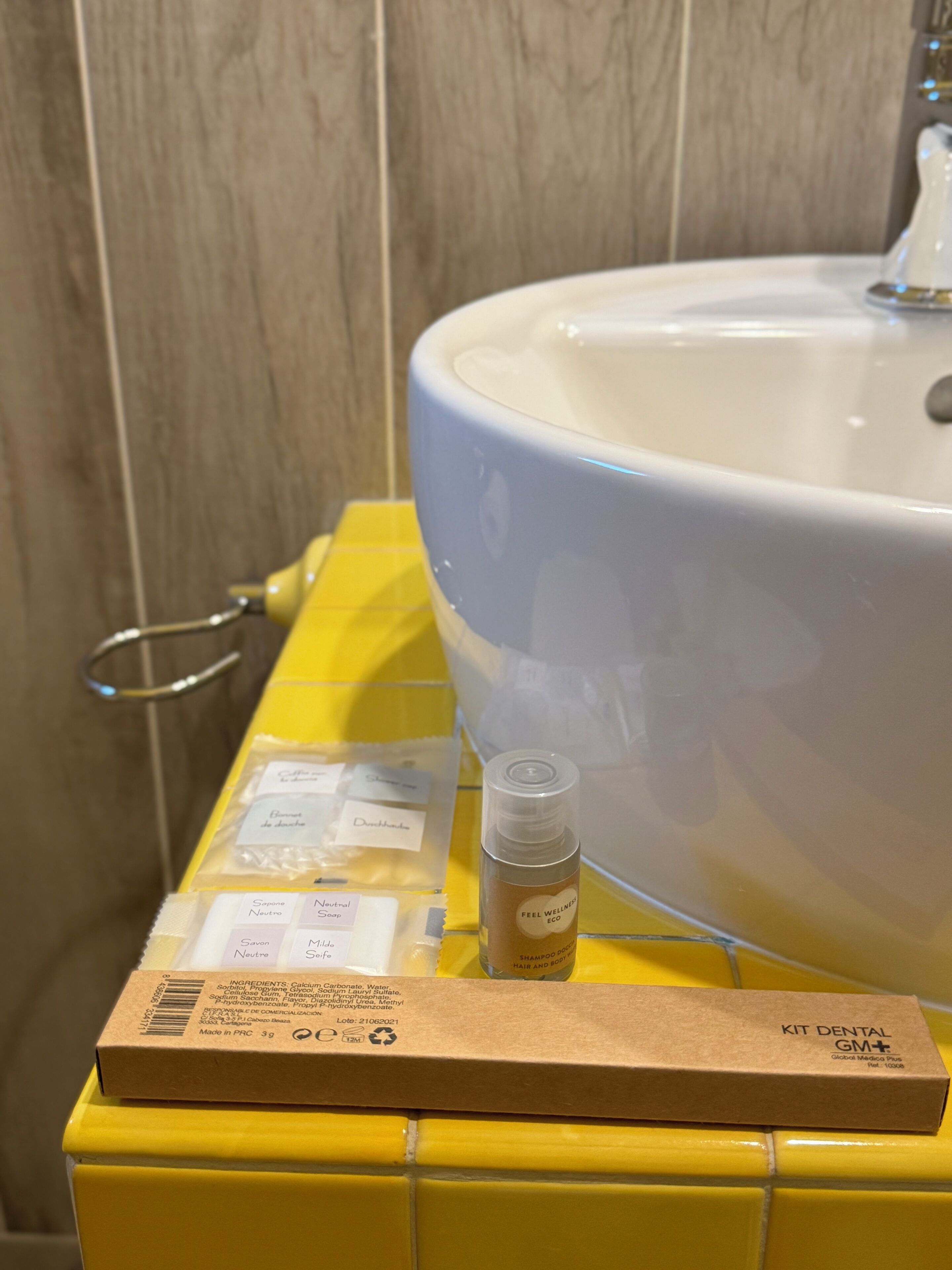 A bathroom with a yellow tiled countertop, a white sink, and a small bottle of shampoo.