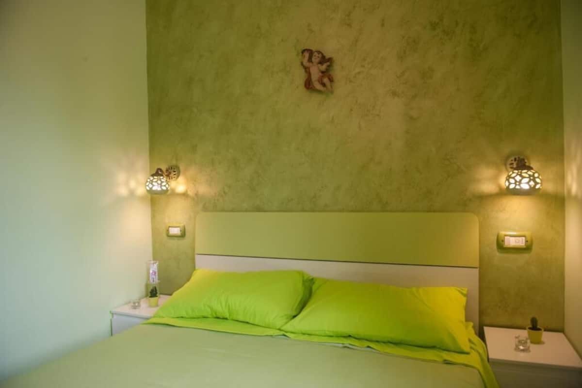 Ein Zimmer mit einem Bett, grünen Kissen und zwei Wandnischen mit Lampen.
