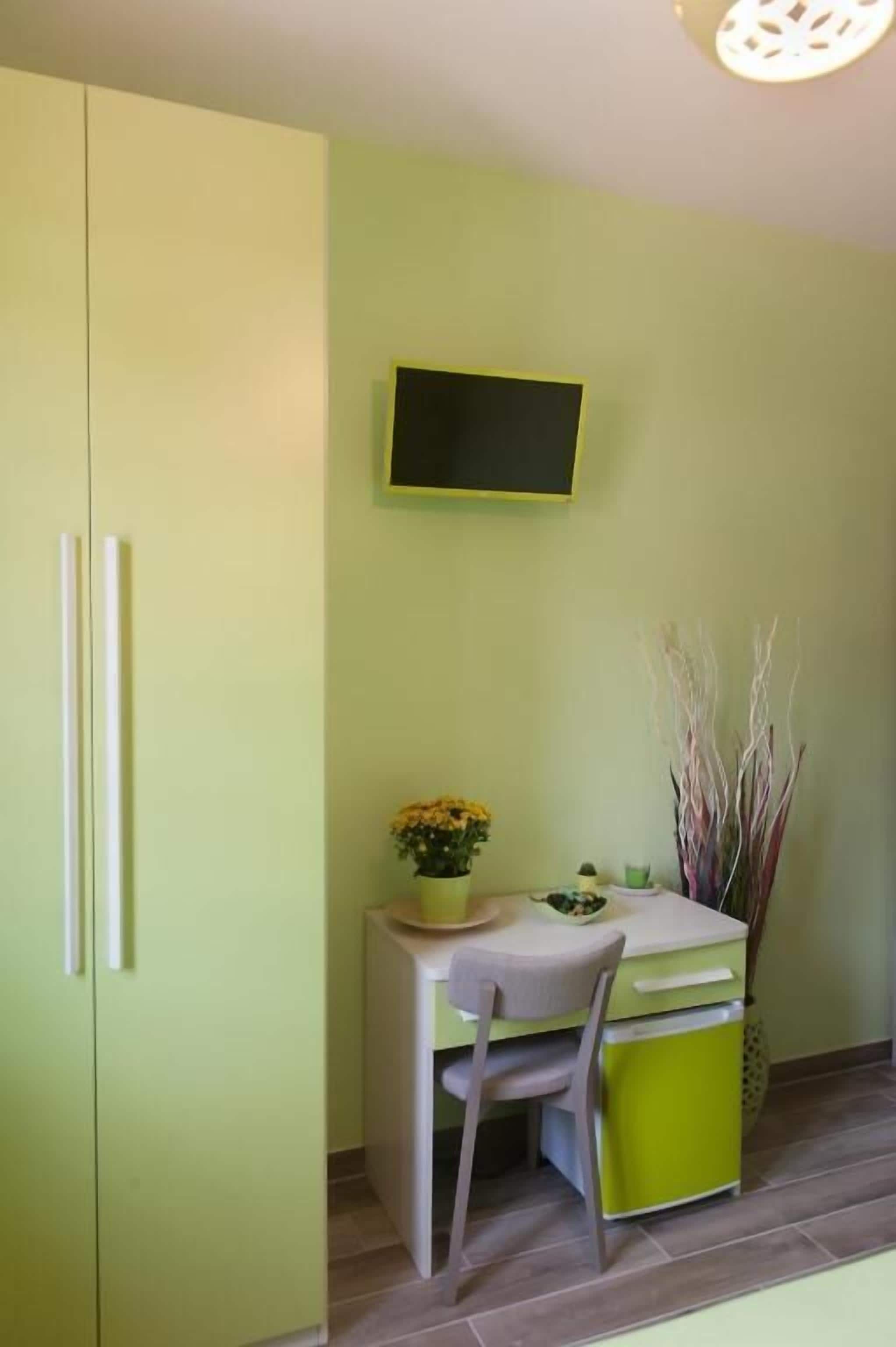 A small kitchen with a green cabinet, a white countertop, a chair, a small table, and a potted plant.