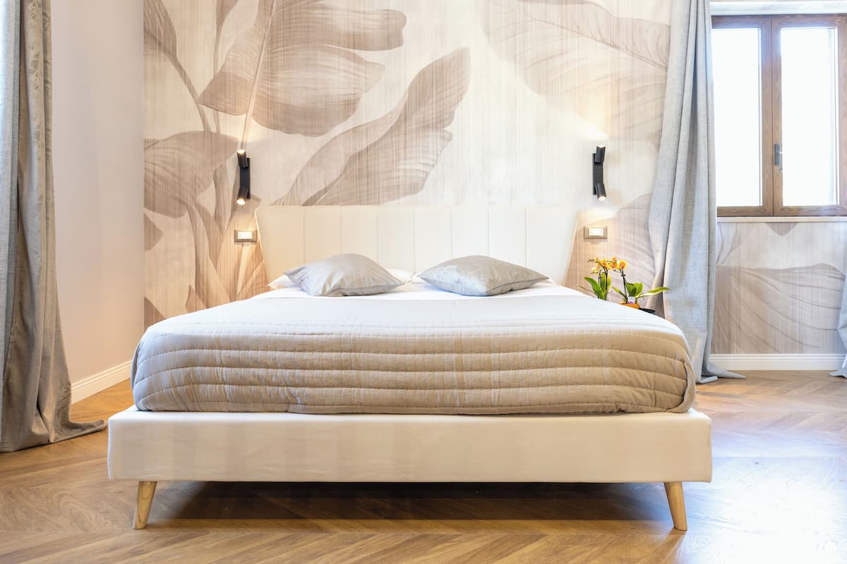Ein Bett mit Holzrahmen und einer beigen, gesteppten Matratze, vor einer Wand mit großem Blattmuster.