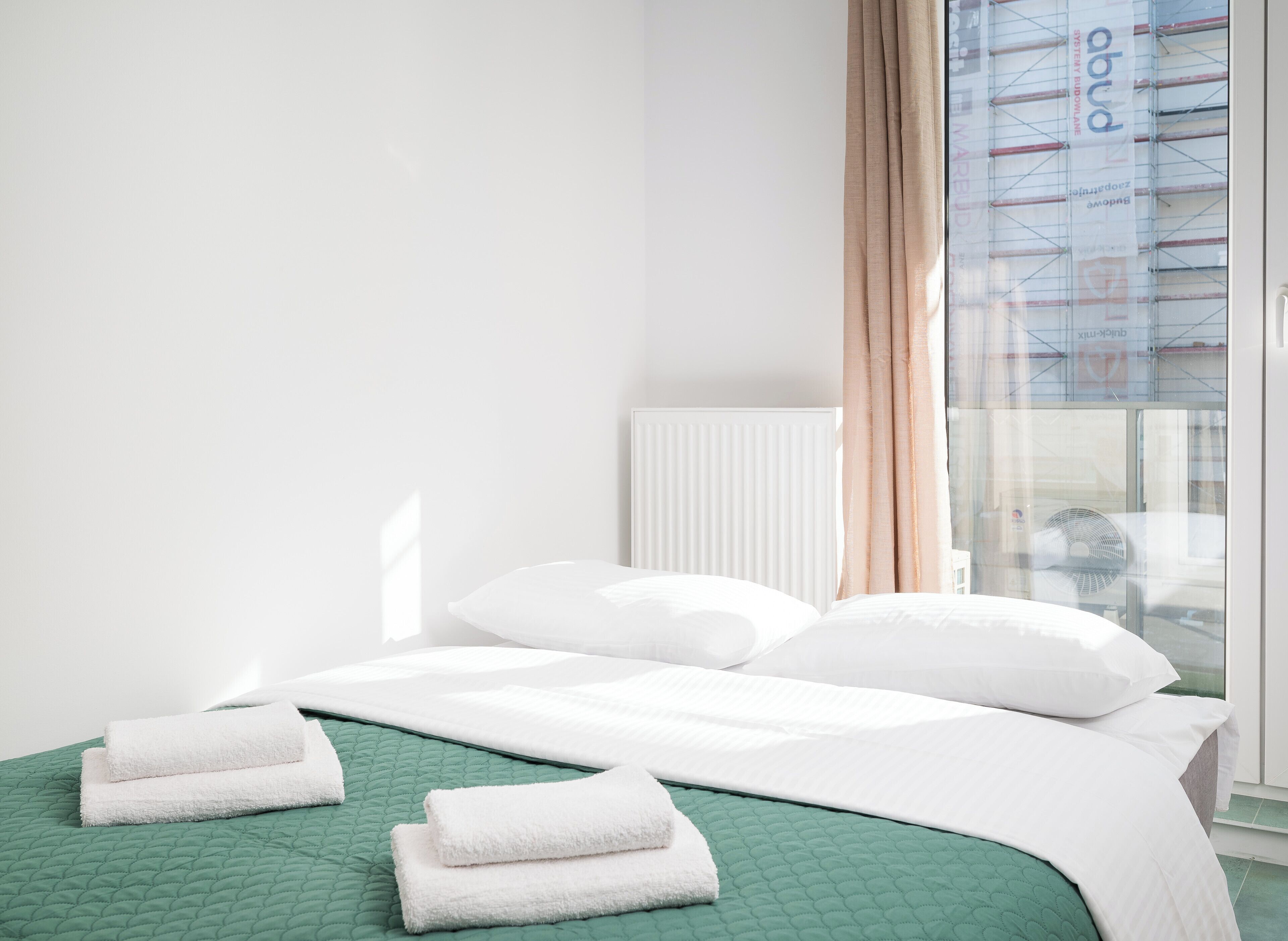 A hotel room with a bed, green bedding, white pillows, and a window with curtains.