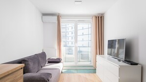 Una sala de estar moderna con un sofá gris, una mesita de madera y un televisor sobre un mueble blanco.