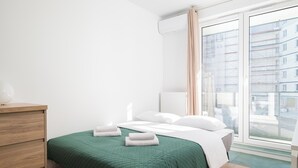 Habitación de hotel con cama, cómoda de madera, radiador y ventana con vistas a edificios.