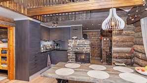 Een moderne keuken met donkere kastjes, een stenen open haard en een houten eettafel met placemats.