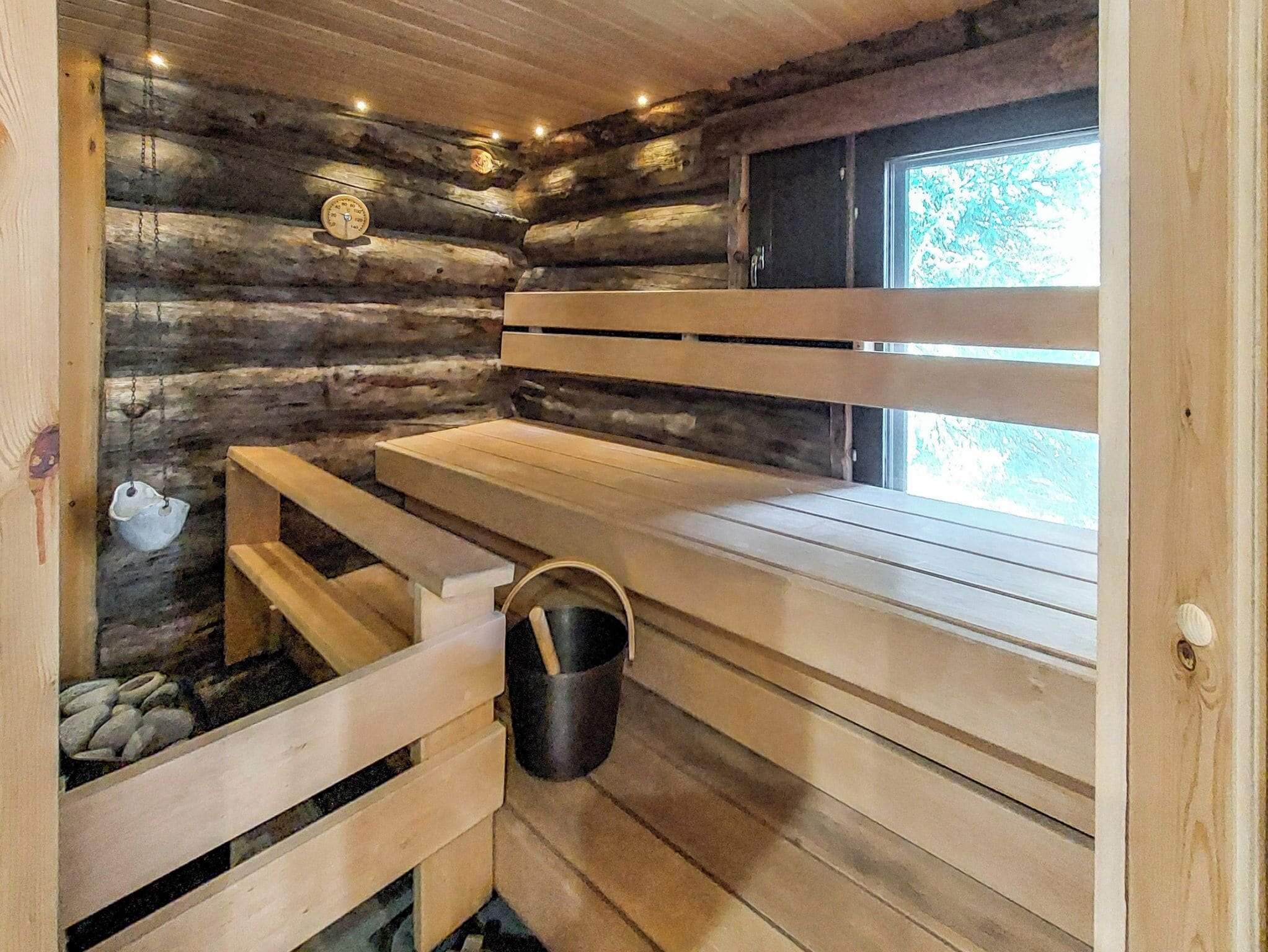 Puisesta laudelavasta ja ikkunasta koostuva sauna, jonka sisustuksessa on käytetty rouheaa hirsiseinää ja siinä on myös kello.