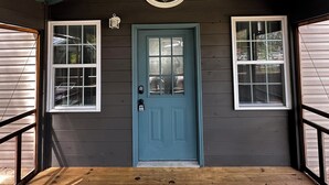 Une porte bleue surmontée d’une fenêtre, flanquée de deux fenêtres avec des volets, et une lanterne au-dessus de la porte.
