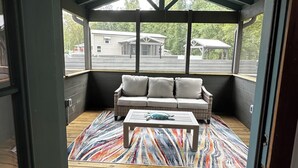 Une véranda couverte avec un plancher en bois, un banc rembourré et un ventilateur de plafond.