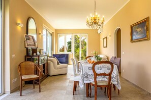 A dining area with a chandelier, dining table, chairs, and a sofa.