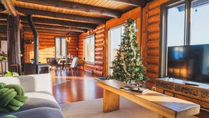 A cozy log cabin interior with a wooden bench, a Christmas tree, a television, and a dining area. - In the heart of nature, with mountain views, ideal for families and pets! (Mandeville)