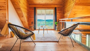 A wooden cabin interior with a dining area, two black chairs, a table, and a view of the outdoors. - In the heart of nature, with mountain views, ideal for families and pets! (Mandeville)