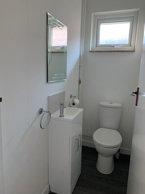 A small, clean bathroom with a white sink, mirror, and toilet. - 3-bed Bungalow Near Hayling Island Sailing Club (Hayling Island)