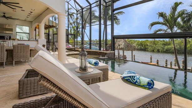 A luxurious indoor pool area with wicker furniture, a glass ceiling, and a view of a natural water body.