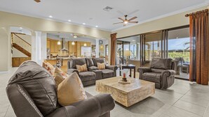 A spacious living room with leather sofas, a wooden coffee table, and a view of the kitchen and outdoor patio.
