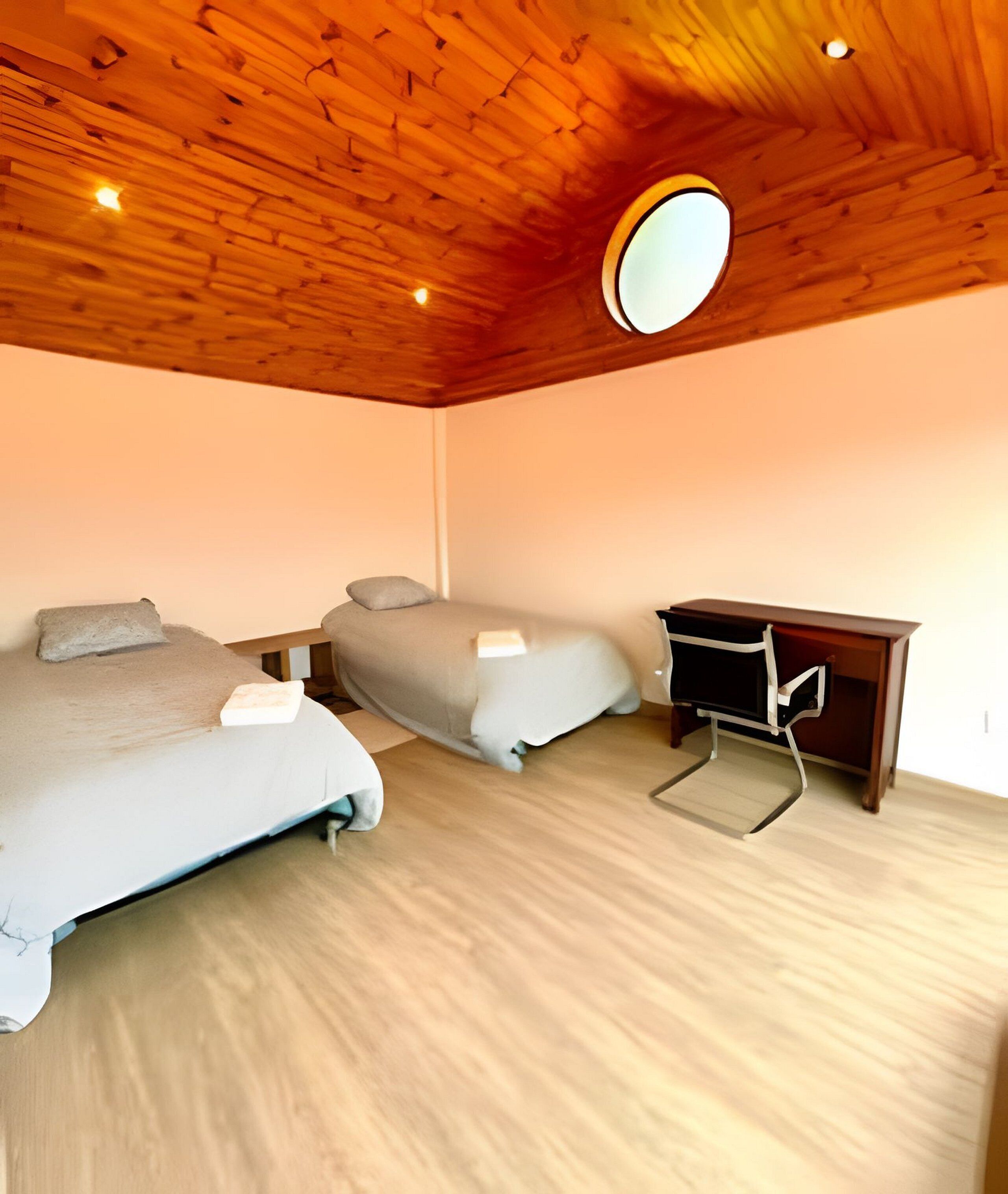 A bedroom with two beds, a wooden ceiling, and a small desk.