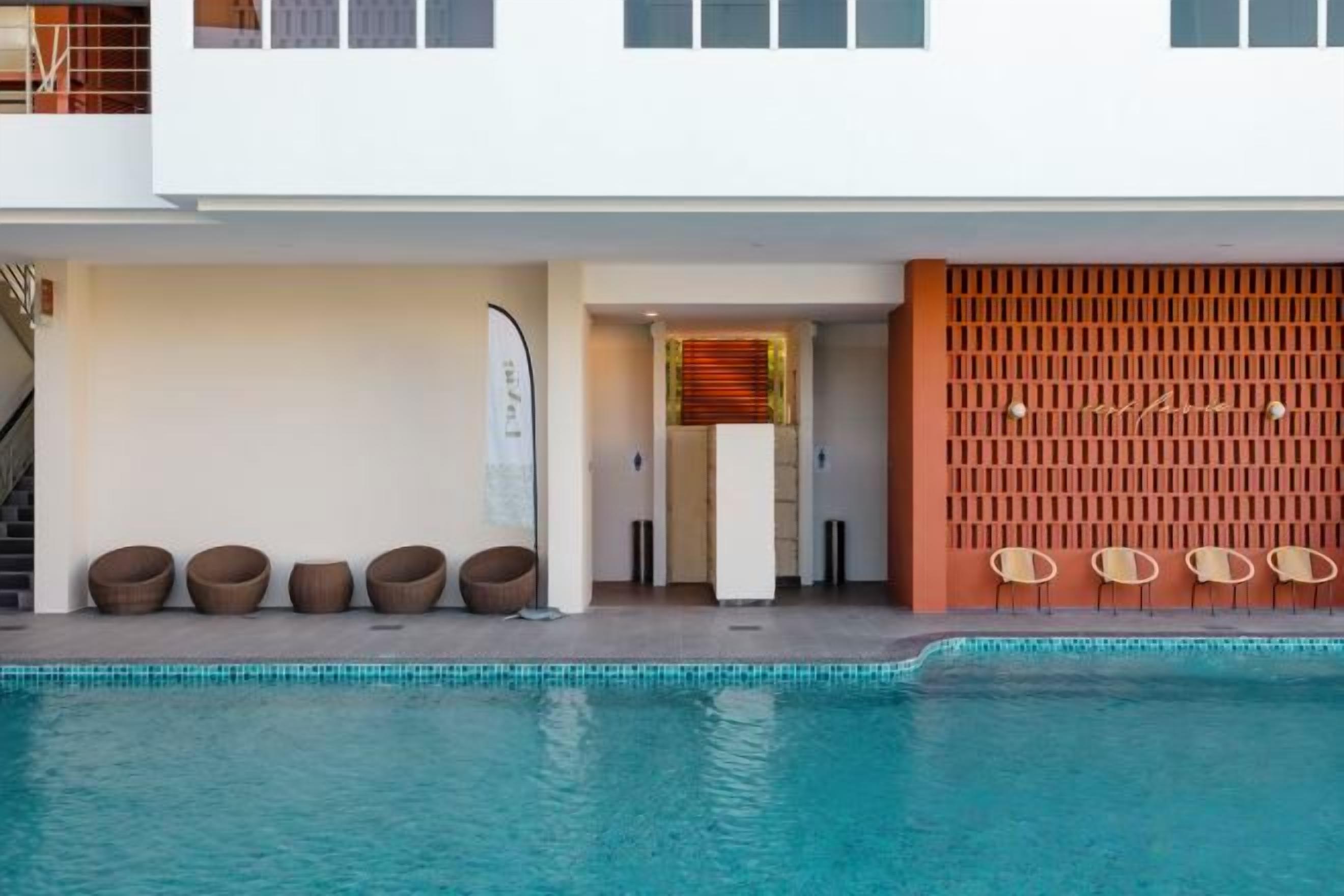 A modern hotel exterior with a swimming pool, outdoor seating, and a covered entrance.