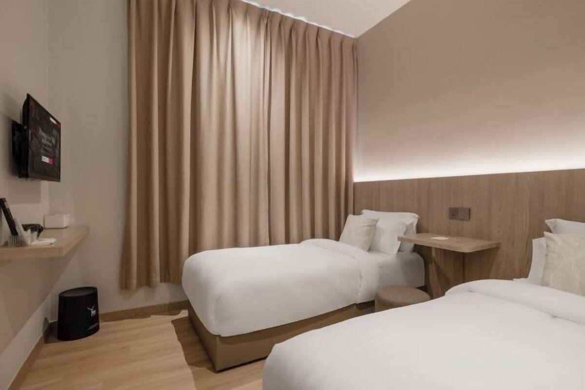 Une chambre d’hôtel avec deux lits, une télévision, une petite table et un rideau.