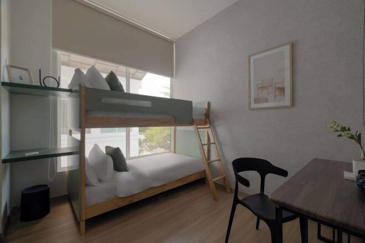 Un lit superposé avec une échelle, un bureau avec une chaise, une fenêtre et un tableau encadré au mur.