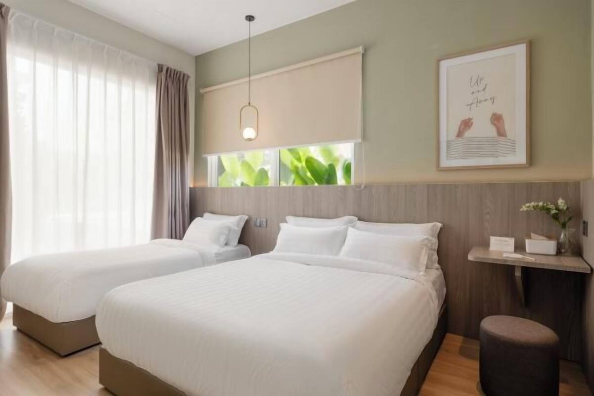 Une chambre d’hôtel avec deux lits, une fenêtre avec des rideaux, une table de chevet avec un vase et un tableau encadré au mur.