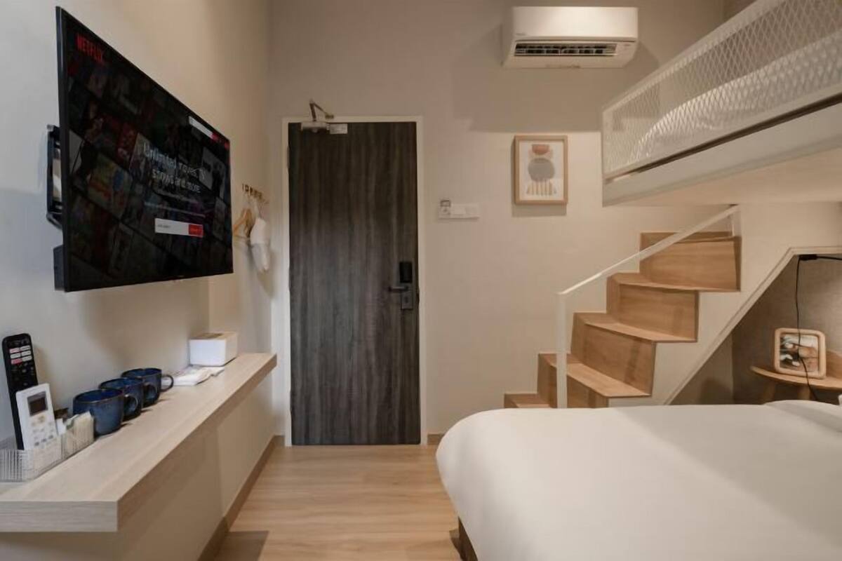 Une chambre d’hôtel avec un lit, un téléviseur fixé au mur, un escalier en bois et une porte.