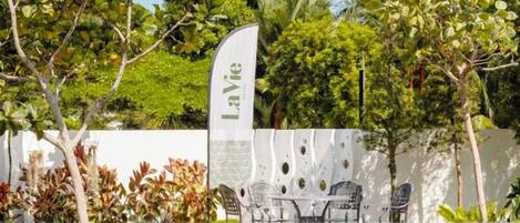 Zona de piscina con una pared blanca, una bandera con el texto 'LaVie' y mobiliario exterior.