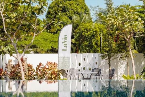 A pool area with a white wall, a flag with 'LaVie' text, and outdoor seating.