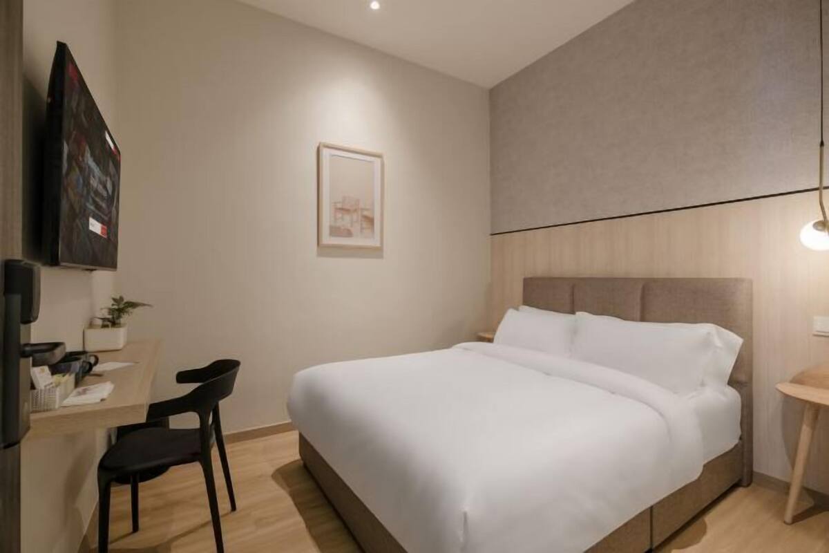 Une chambre d’hôtel moderne équipée d’un lit, d’un bureau avec une chaise, d’une petite table et d’un téléviseur fixé au mur.