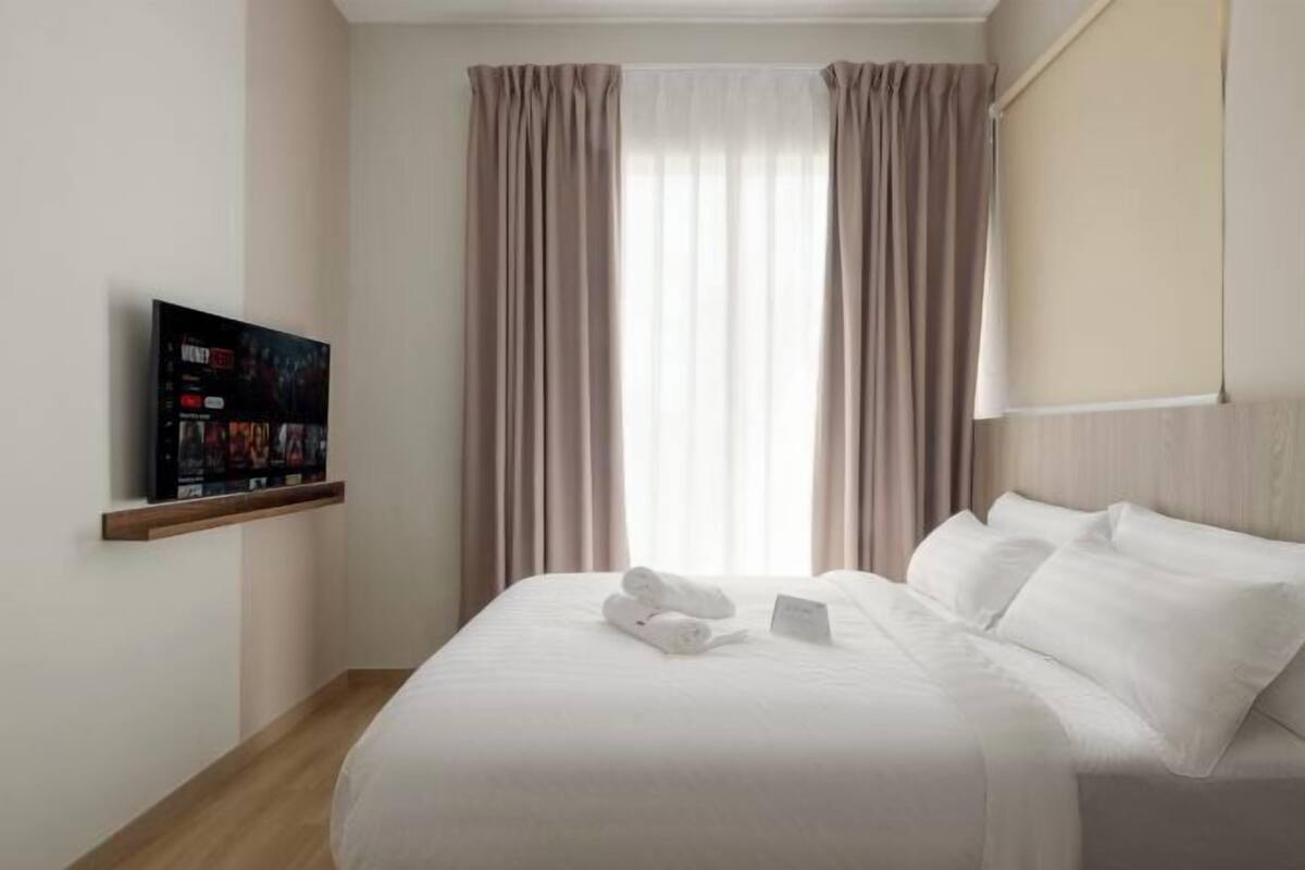 Une chambre d’hôtel avec un lit, un téléviseur posé sur une étagère et des rideaux.