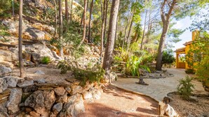 A stone pathway leading through a forested area with a stone wall and a yellow building in the background. - Villa 'Macondo Altea Hills' with Sea View, Wi-Fi and Air Conditioning (Altea)