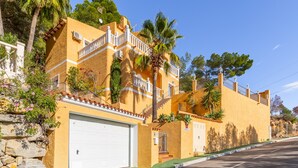 A yellow building with a white garage door, balconies, and a stone wall. - Villa 'Macondo Altea Hills' with Sea View, Wi-Fi and Air Conditioning (Altea)