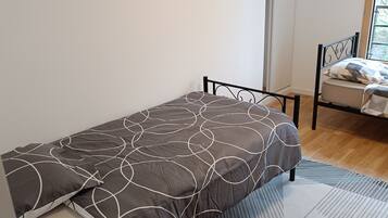 A single bed with a patterned bedspread, a metal headboard, and a geometric rug on a wooden floor.
