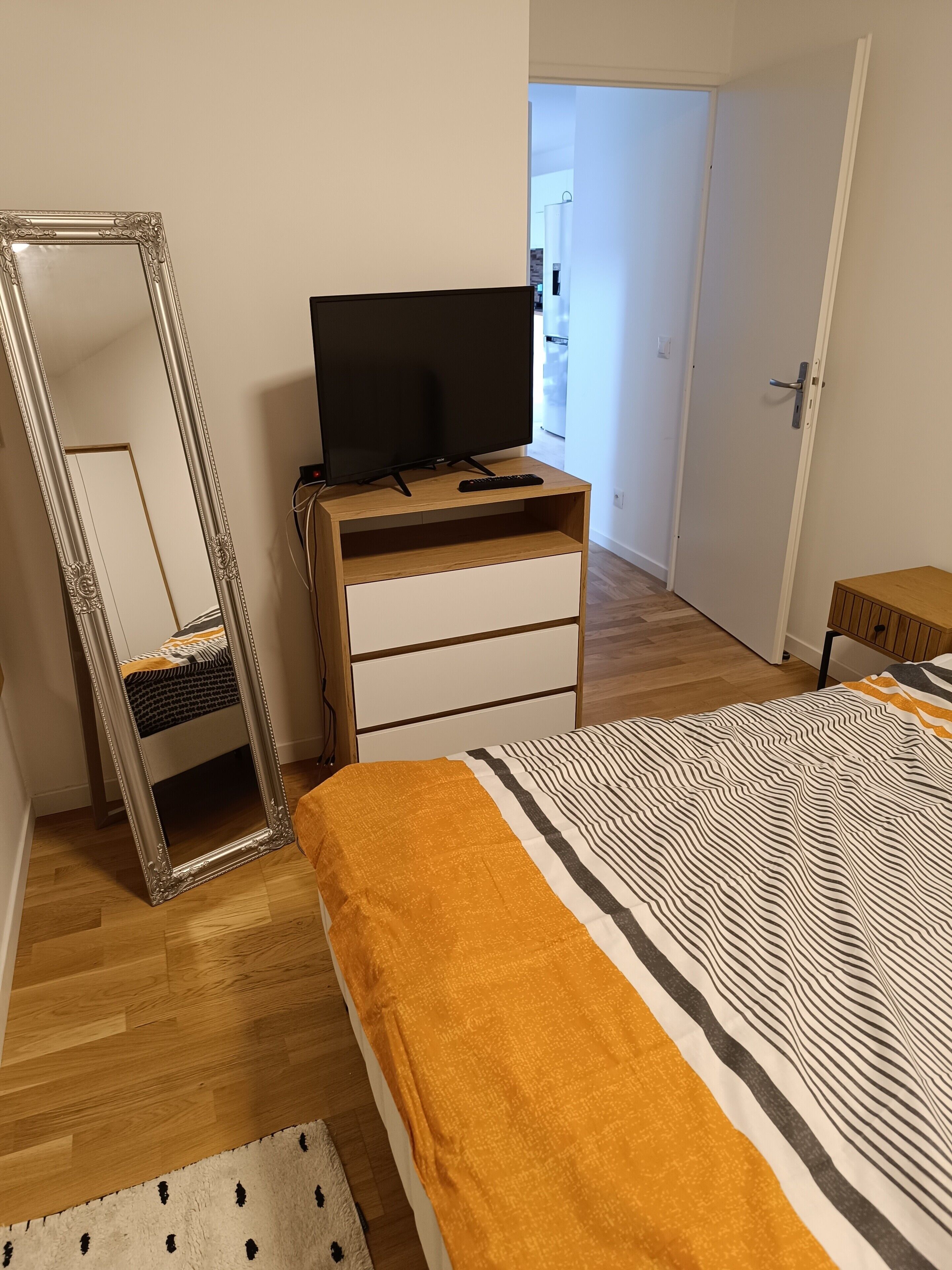 A bedroom with a bed, a dresser, a television, and a mirror.