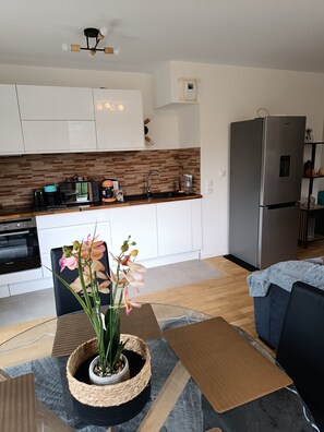 A modern kitchen with white cabinets, a stainless steel refrigerator, and a coffee maker. - Apartment 'Chez Sibylle Chevreuse Saclay' with Balcony, Wi-Fi and Air Conditioning (Saint-Rémy-lès-Chevreuse)