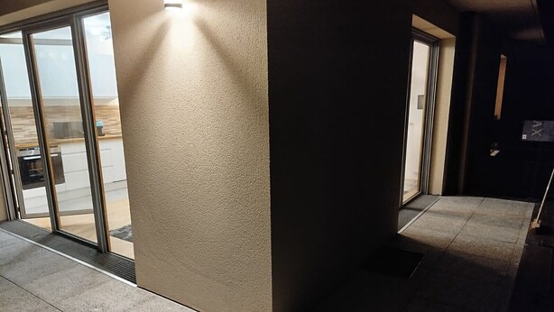 Un pasillo con pared texturizada, una puerta de cristal que da a una zona de cocina y suelo de baldosas.