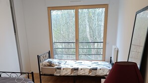 Un dormitorio con cama, una silla, una lámpara y una ventana con vistas a árboles.
