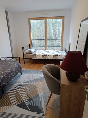 Ein Schlafzimmer mit Bett, Stuhl, Lampe und Fenster mit Blick auf Bäume.