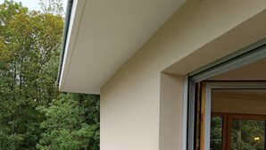 Un edificio moderno con balcón, puerta de cristal y vista a zona boscosa.