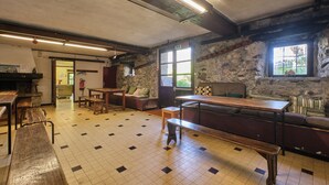 Una habitación con suelo de baldosas, bancos de madera, una mesa larga y una pared de piedra.
