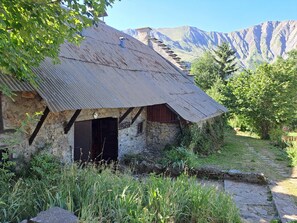 Un edificio rustico in pietra con tetto in lamiera ondulata, una porta in legno e una scalinata in pietra che conduce a una piattaforma.