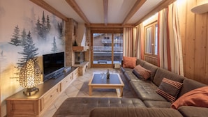 Un salon avec une cheminée, un téléviseur, un canapé et une vue sur un immeuble, visible à travers une porte vitrée.