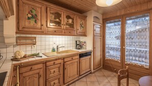 Une cuisine avec des meubles de rangement en bois, un évier et une fenêtre ornée de rideaux en dentelle.