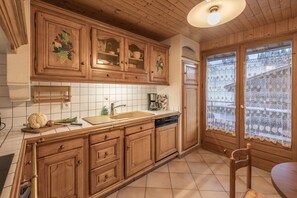 Una cocina con armarios de madera, un lavabo y un ventanal con cortinas de encaje.