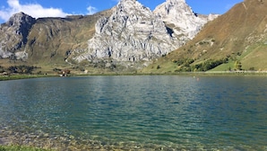 Un paysage de montagne avec un lac aux eaux claires, un terrain rocheux et un petit bâtiment situé près du bord de l’eau.