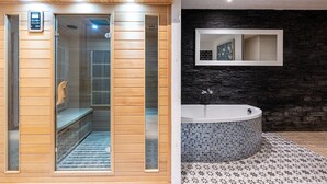 A sauna with a wooden exterior and glass doors, a black stone wall, a tiled floor, and a large bathtub.