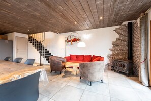 A modern living room with a wooden ceiling, a fireplace, a dining table, and a sofa.